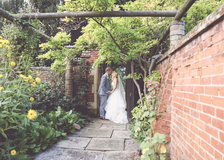 A bride and groom kissing in the doorway in the garden on a wedding day at Lanwades Hall in Suffolk captured by Suffolk Wedding Photographer Hayley Denston Photography