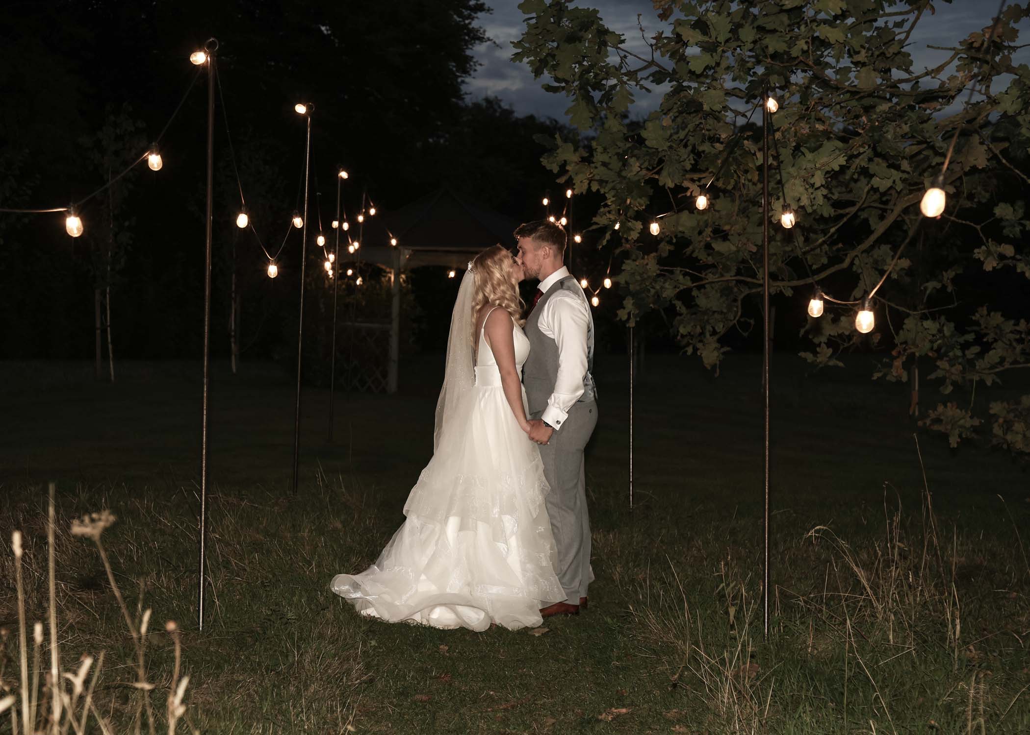 A bride and groom kissing amongst a festoon of lights on a wedding day at Lanwades Hall in Suffolk captured by Suffolk Wedding Photographer Hayley Denston Photography