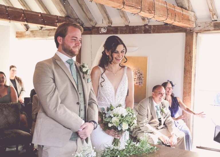 A bride and groom laughing during their wedding ceremony on a wedding day at Tuddenham Mill in Suffolk Captured by Suffolk Wedding Photographer Hayley Denston Photography