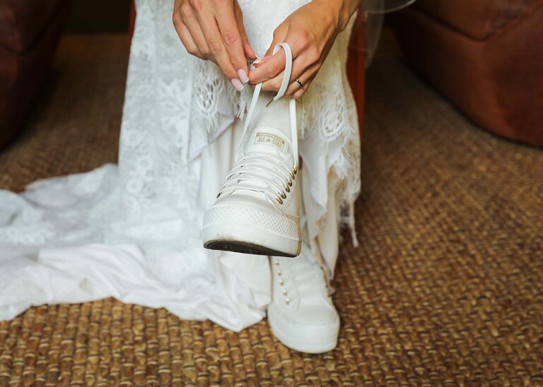A close up of a bride putting on her white converse wedding trainers on her wedding day at Tuddenham Mill in Suffolk Captured by Suffolk Wedding Photographer Hayley Denston Photography