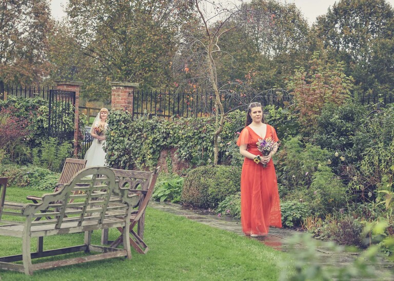 A bridesmaid walking down a garden path to a wedding ceremony on a wedding day at the Garden Barn, Little Bradley captured by Hayley Denston Photography