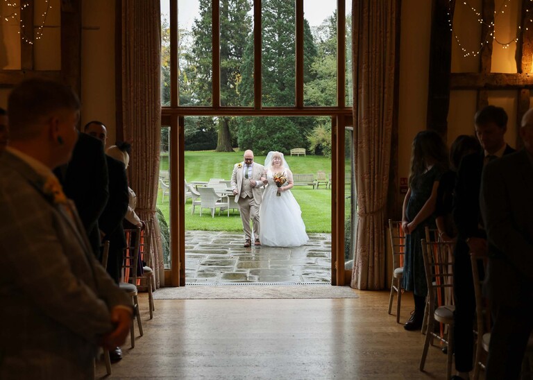 A bride and her dad stood arm in arm with the garden behind them before walking down the aisle on a wedding day at the Garden Barn, Little Bradley captured by Hayley Denston Photography