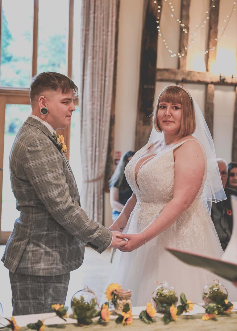 A bride and groom holding hands and looking at the registrar on a wedding day at the Garden Barn, Little Bradley captured by Hayley Denston Photography