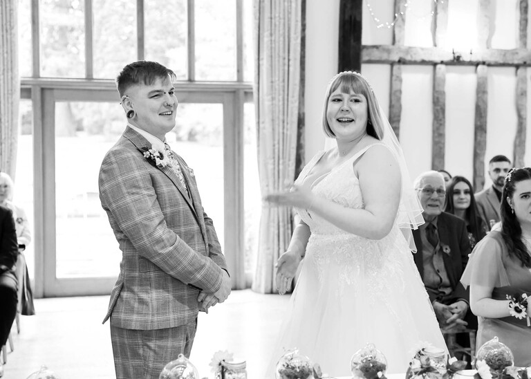 A black and white photo of a bride and groom laughing during their wedding ceremony on a wedding day at the Garden Barn, Little Bradley captured by Hayley Denston Photography