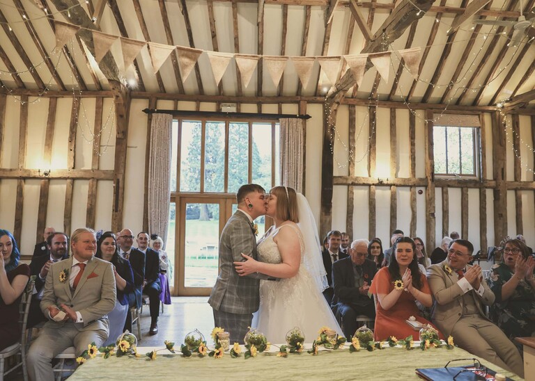 A bride and groom kissing in front of their guests as they become husband and wife at their wedding ceremony on a wedding day at the Garden Barn, Little Bradley captured by Hayley Denston Photography