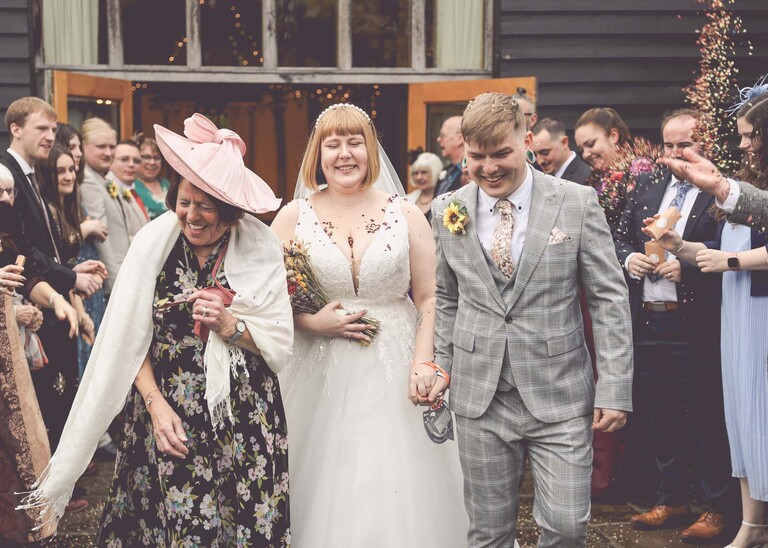 A grandma throwing confetti over a bride and groom on a wedding day at the Garden Barn, Little Bradley captured by Hayley Denston Photography