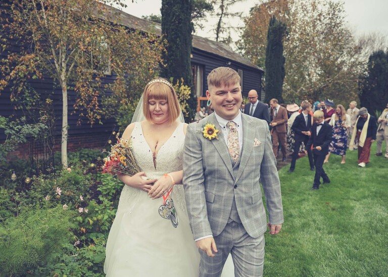 A bride and groom laughing and leading their guests to reception on a wedding day at the Garden Barn, Little Bradley captured by Hayley Denston Photography