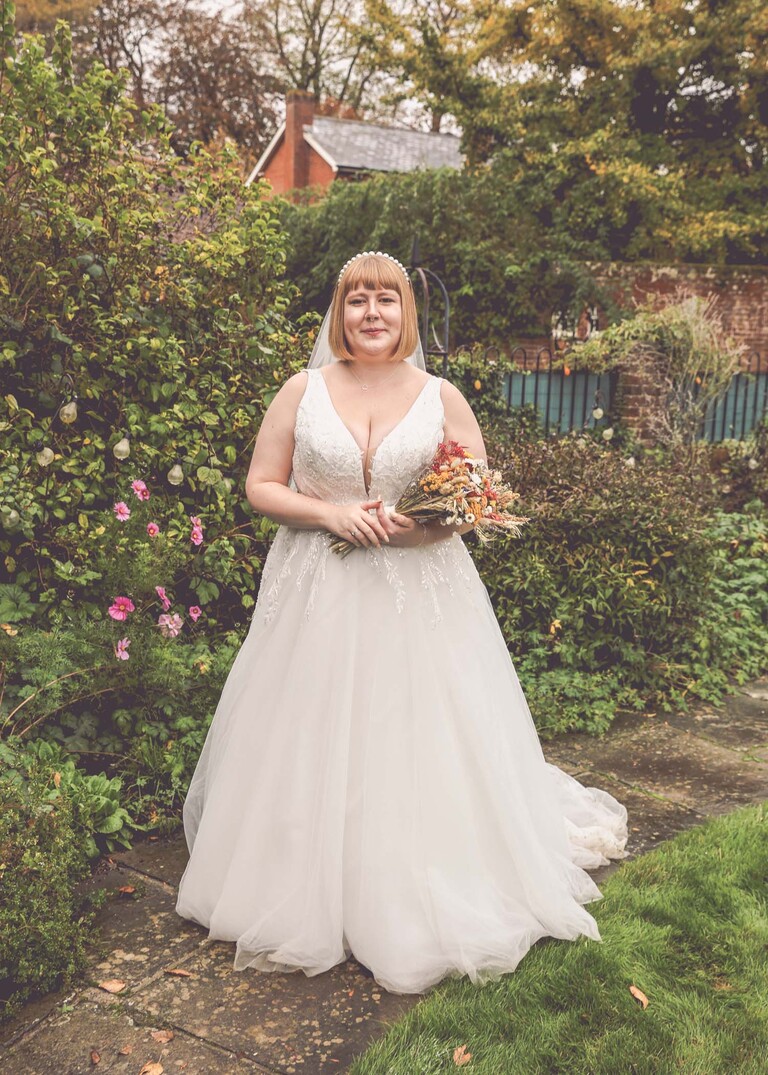 A bridal portrait of a bride stood with her bouquet surrounded by gardens on a wedding day at the Garden Barn, Little Bradley captured by Hayley Denston Photography