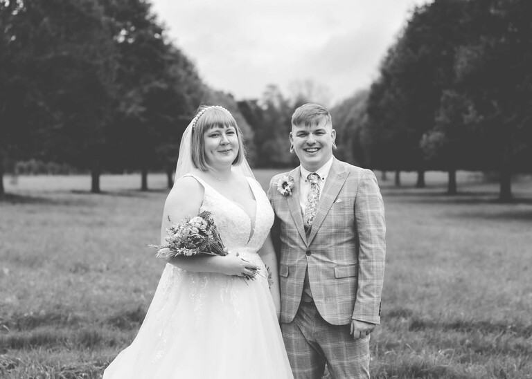 A black and white photo of a bride and groom stood in front of a tree lined avenue on their wedding day at the Garden Barn, Little Bradley captured by Hayley Denston Photography