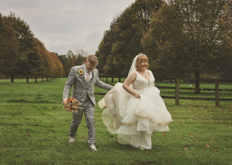 A bride and groom walking in front of a tree lined avenue on their wedding day at the Garden Barn, Little Bradley captured by Hayley Denston Photography