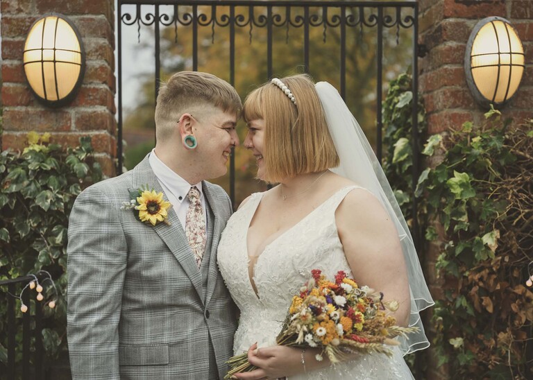 A bride and groom looking at each other in front of a wrought iron gate with their noses touching on their wedding day at the Garden Barn, Little Bradley captured by Hayley Denston Photography
