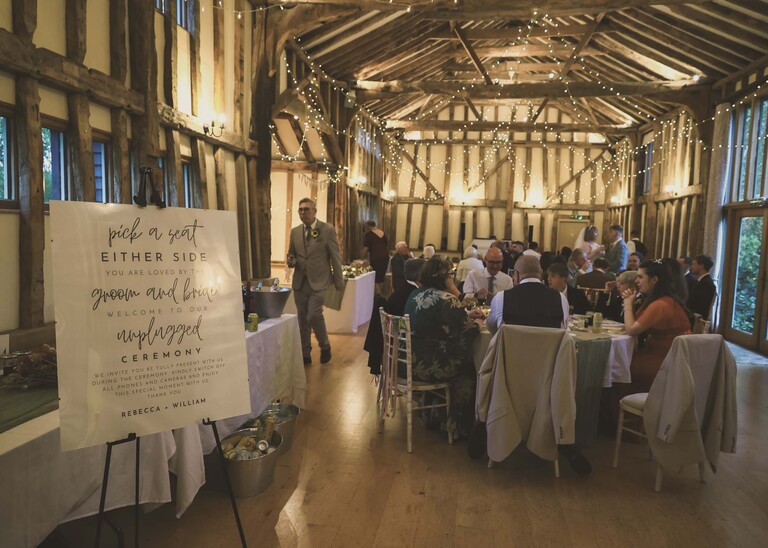 The inside of a barn all decorated for a wedding breakfast with guests sat at the tables on a wedding day at the Garden Barn, Little Bradley captured by Hayley Denston Photography