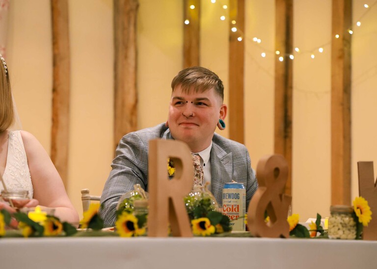A groom sat at his table listening to the father of the bride speech on his wedding day at the Garden Barn, Little Bradley captured by Hayley Denston Photography