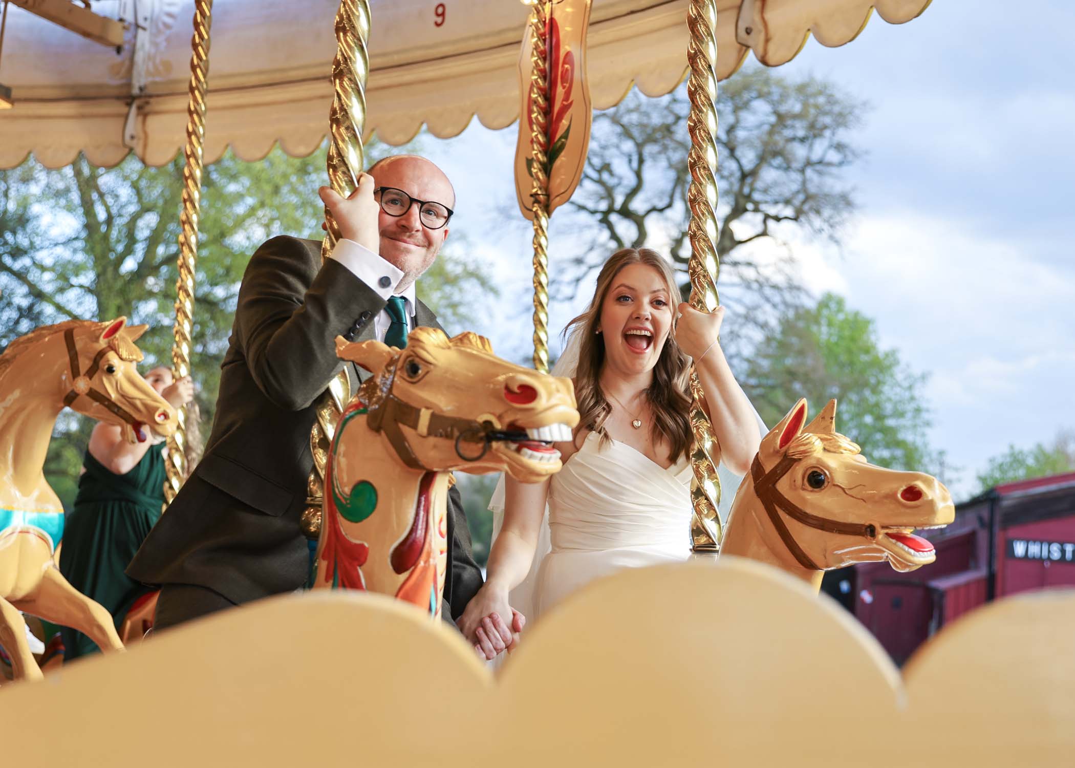 A bride and groom riding two horses on a carousel on a wedding day at Bressingham Hall photographed by Suffolk Wedding Photographer Hayley Denston Photography