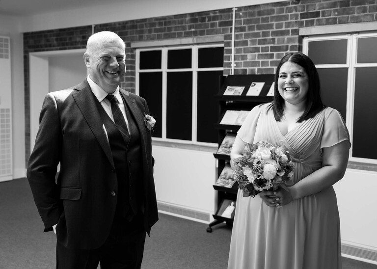 A black and white photo of a father of the bride and bridesmaid laughing together photographed by Suffolk Wedding Photographer Hayley Denston Photography
