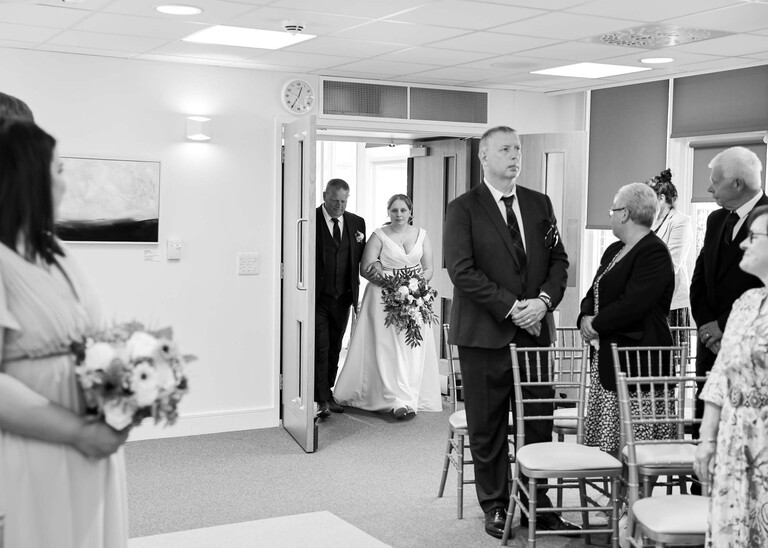 A black and white photo of a bride and her dad walking down the aisle photographed by Suffolk Wedding Photographer Hayley Denston Photography