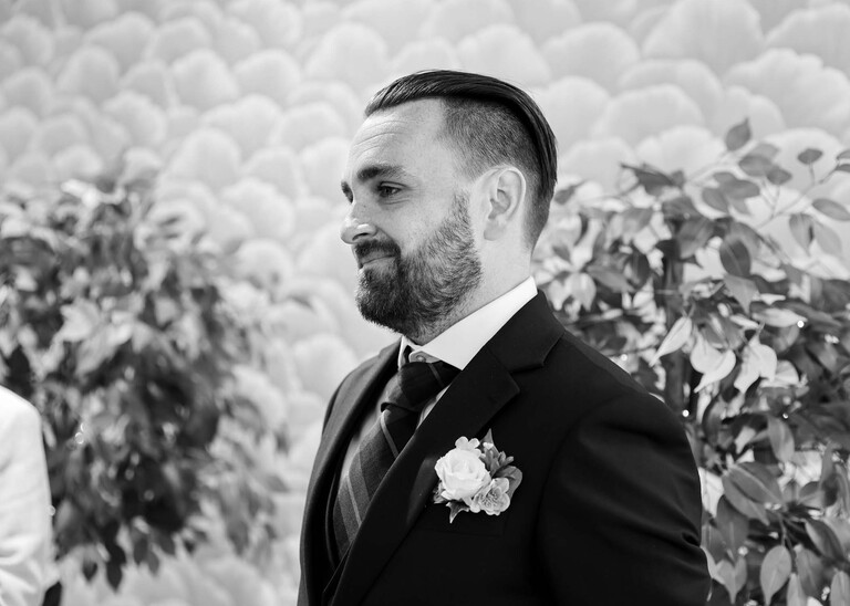 A black and white photo of a bearded groom looking at his bride walking down the aisle photographed by Suffolk Wedding Photographer Hayley Denston Photography