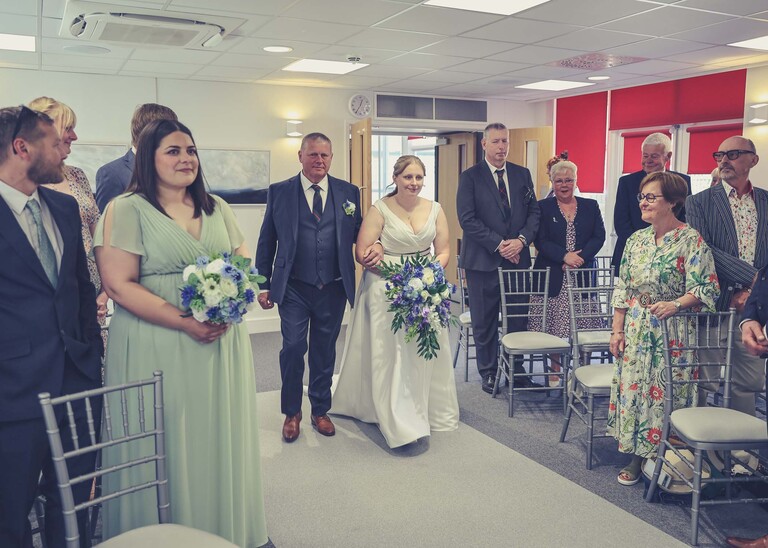 A bride and her dad walking down the aisle at Cambridge Registry Office photographed by Suffolk Wedding Photographer Hayley Denston Photography