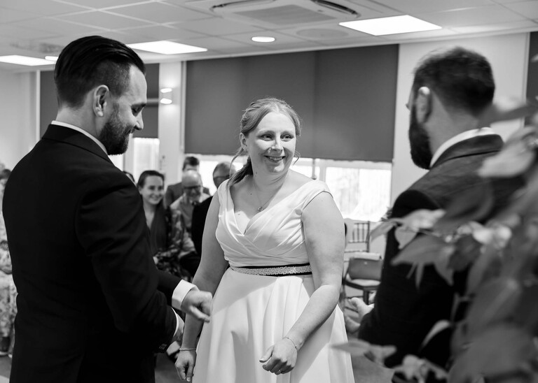 A black and white photo of a bride laughing at the bestman during a  wedding ceremony at Cambridge Registry Office photographed by Suffolk Wedding Photographer Hayley Denston Photography