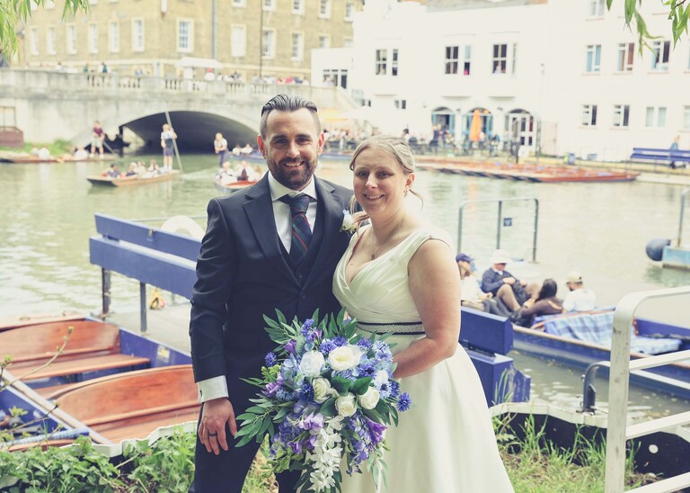 A photo of a bride and groom stood with punts behind them at Cambridge Mill Pond on their wedding day photographed by Suffolk Wedding Photographer Hayley Denston Photography