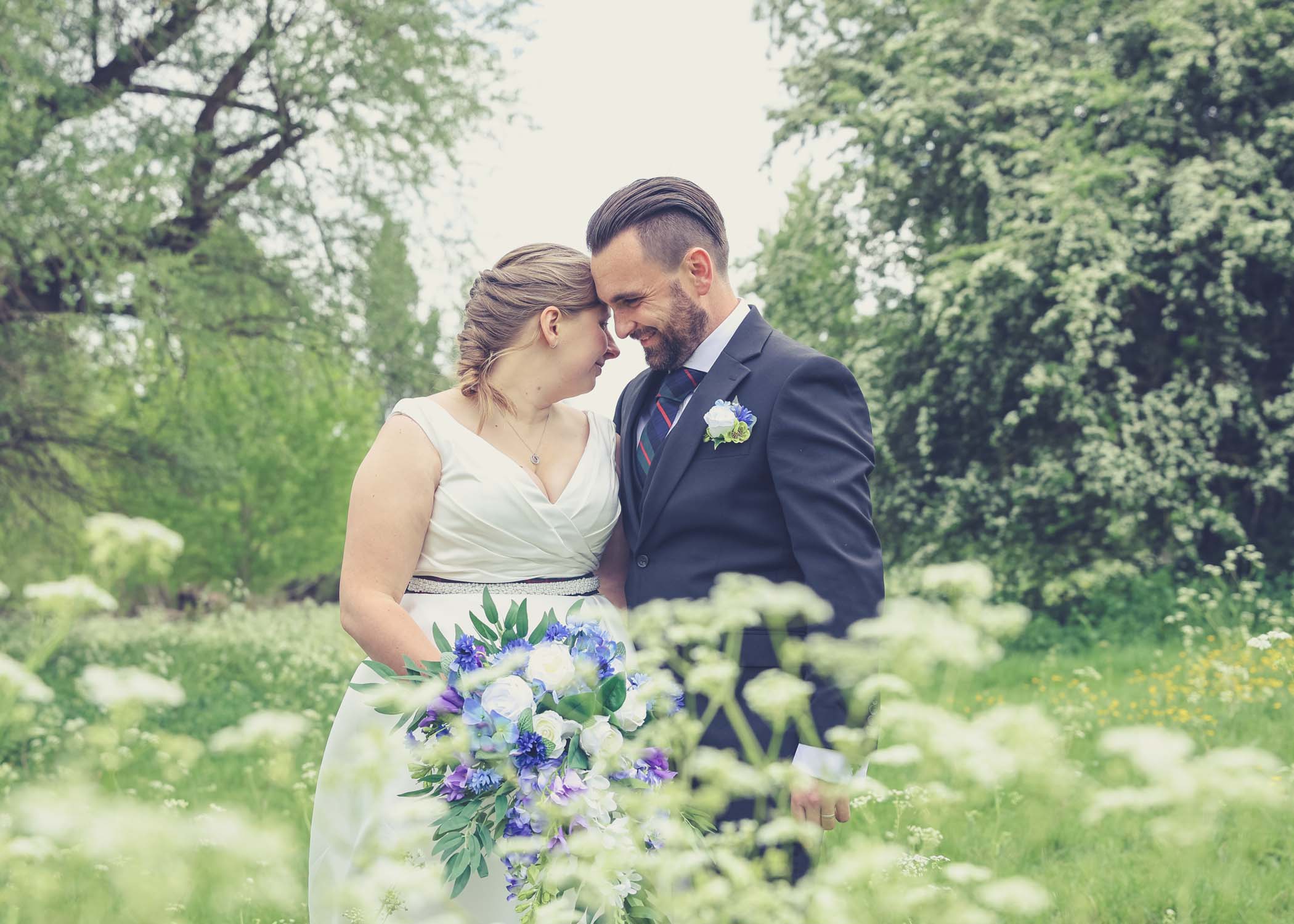 A bride and groom leaning in to each other surrounded by cow parsley in Meadows down at Cambridge Mill Pond on their wedding day photographed by Suffolk Wedding Photographer Hayley Denston Photography