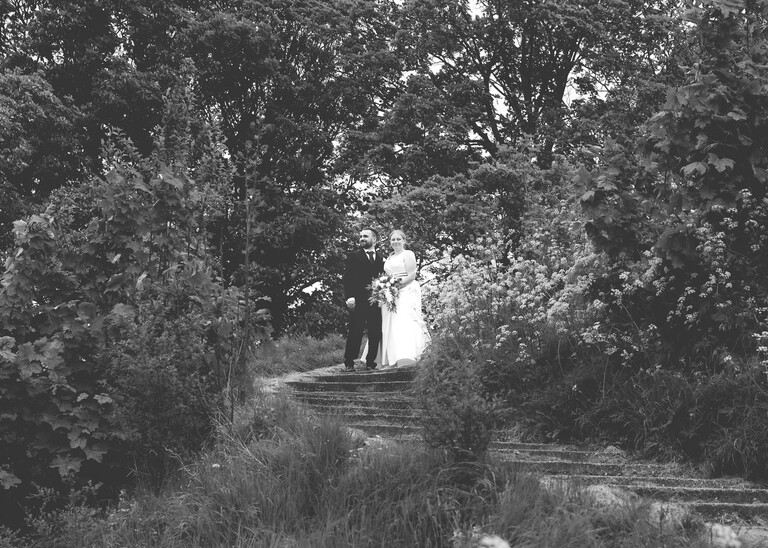 A black and white photo of a bride and groom walking up Castle Hill in Cambridge on their wedding day photographed by Suffolk Wedding Photographer Hayley Denston Photography