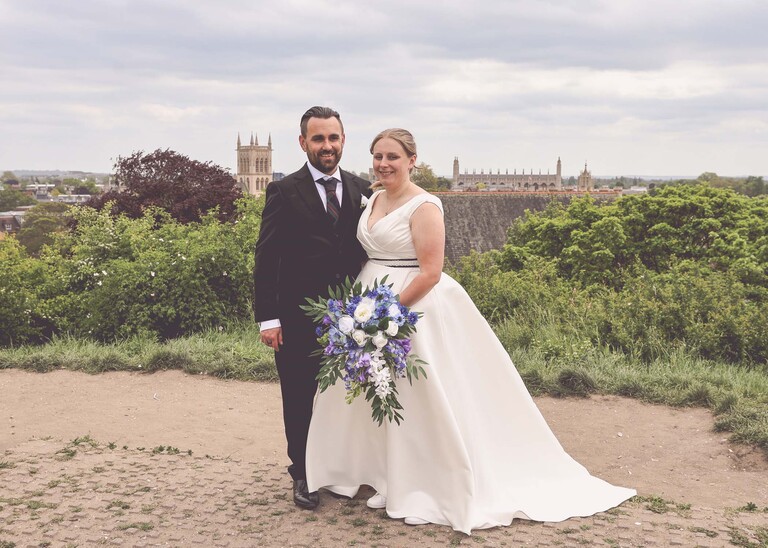 A bride and groom stood at the top of  Castle Hill in Cambridge on their wedding day with kings college and the city behind them  photographed by Suffolk Wedding Photographer Hayley Denston Photography