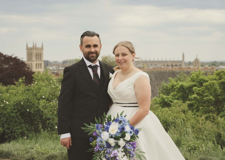 A bride and groom stood at the top of  Castle Hill in Cambridge on their wedding day with kings college and the city behind them  photographed by Suffolk Wedding Photographer Hayley Denston Photography