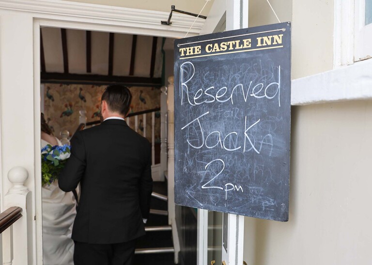 A bride and groom walking in to their wedding reception at the castle inn in Cambridge with a reserved sign up photographed by Suffolk Wedding Photographer Hayley Denston Photography