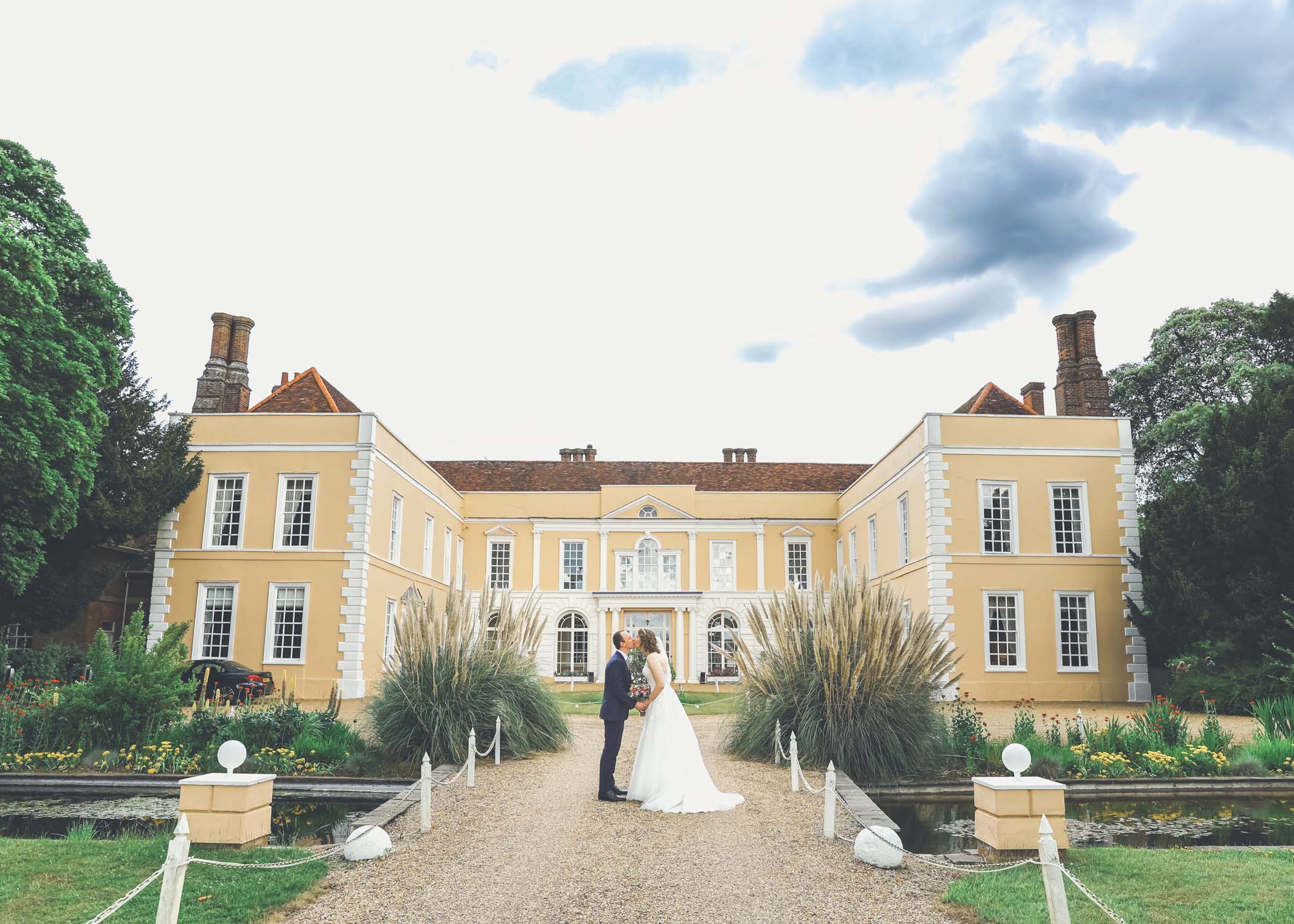 A bride and groom kissing in front of a grand georgian building at Hintlesham Hall on a wedding day captured by Suffolk Wedding Photographer Hayley Denston Photography