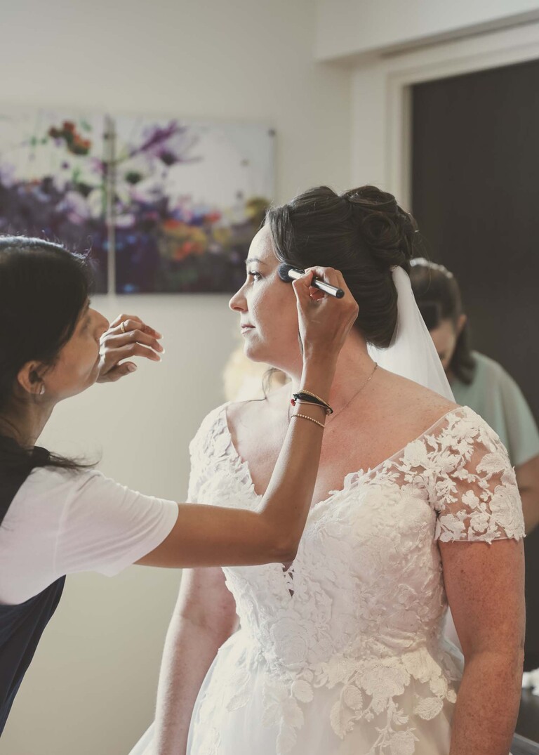 A MUA putting blusher on the bride on a wedding day captured by suffolk wedding Photographer Hayley Denston Photography
