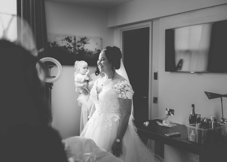 A black and white photo of a bride smiling in a hotel room on a wedding day captured by suffolk wedding Photographer Hayley Denston Photography