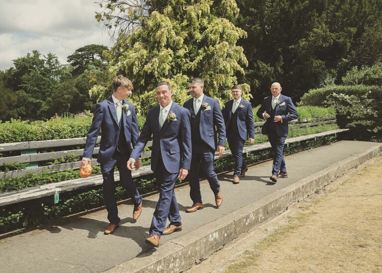 A groom and his groomsmen walking through the abbey gardens in bury st edmunds on a wedding day captured by suffolk wedding Photographer Hayley Denston Photography