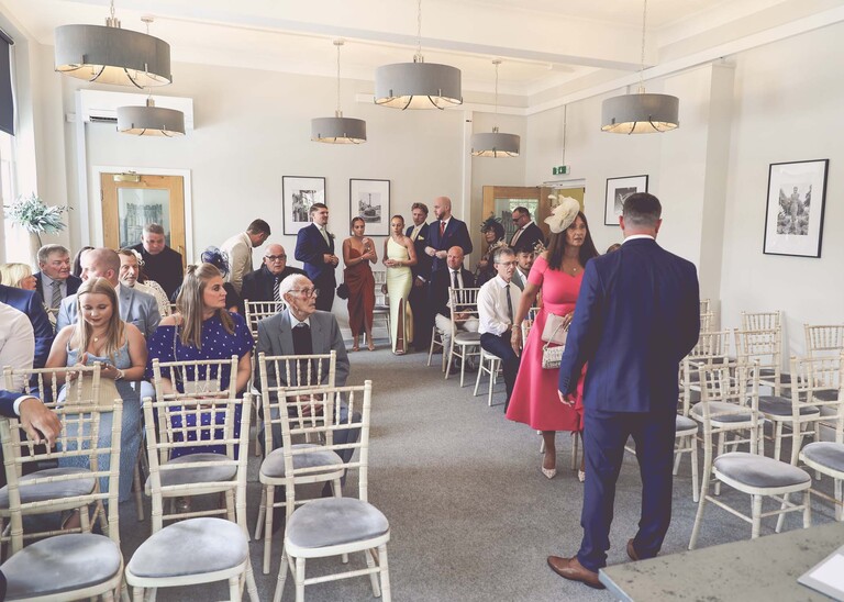 A groom and guests getting seated in the wedding ceremony room in bury st edmunds on a wedding day captured by suffolk wedding Photographer Hayley Denston Photography