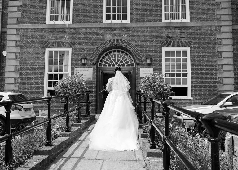 A black and white photo of a bride from behind walking in to bury st edmunds registry office on a wedding day captured by suffolk wedding Photographer Hayley Denston Photography