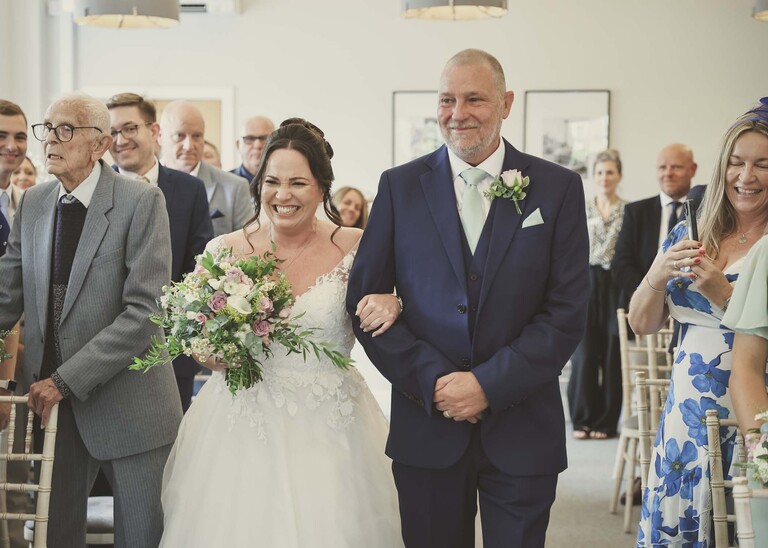 A bride and her dad walking down the aisle at bury st edmunds registry office on a wedding day captured by suffolk wedding photographer Hayley Denston Photography