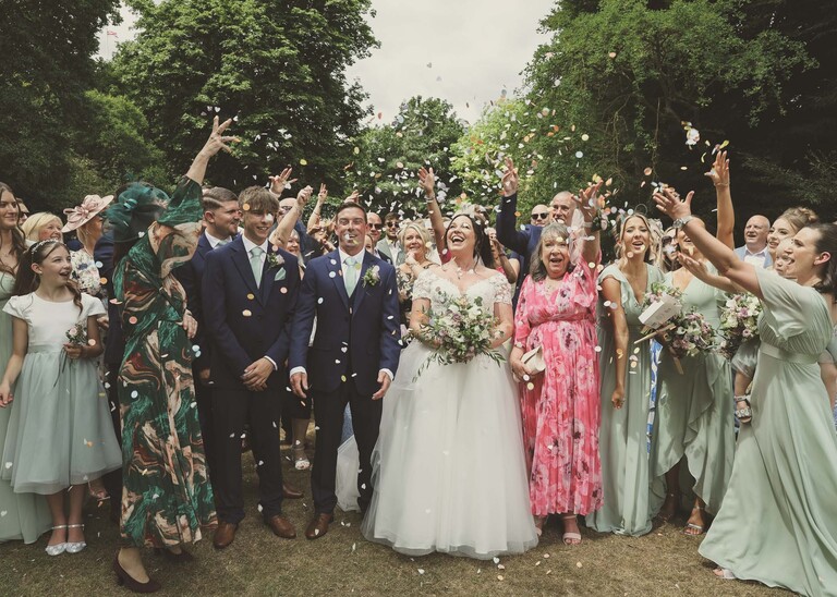 A bride and groom with guests throwing confetti over them in bury st edmunds abbey gardens on a wedding day captured by suffolk wedding photographer Hayley Denston Photography