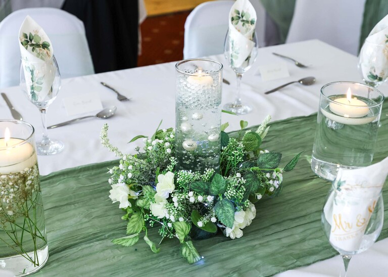 A candle floating in a vase of water surrounded by flowers at Mildenhall Social Club for a wedding reception captured by Suffolk Wedding Photographer Hayley Denston Photography