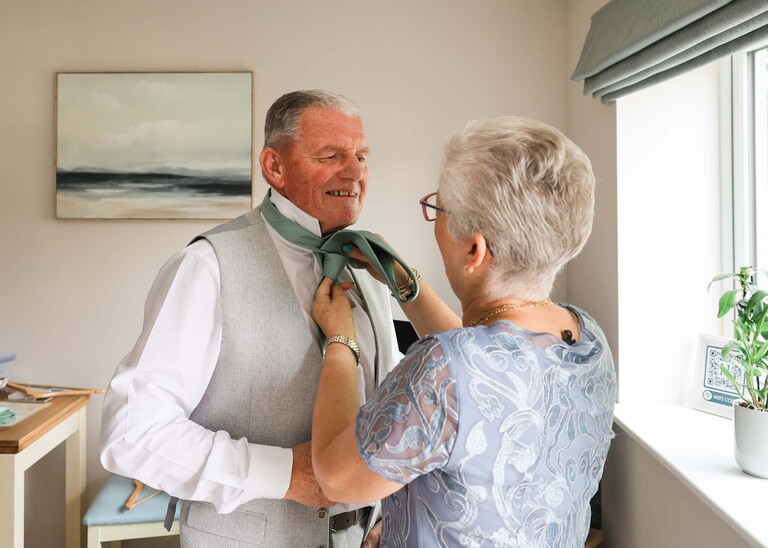 A father of the bride having his tie done up by his wife on a wedding day at Hungarian Hall Estate captured by Suffolk Wedding Photographer Hayley Denston Photography