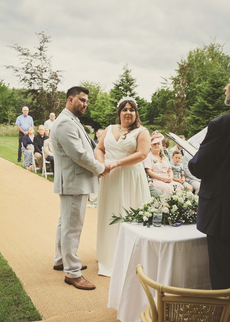A bride and groom holding hands during their outdoor wedding ceremony on a wedding day at Hungarian Hall Estate captured by Suffolk Wedding Photographer Hayley Denston Photography