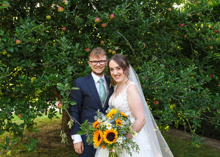 A bride and groom stood in front of an apple tree on a wedding day at Applewood Hall in Norfolk captured by suffolk and norfolk wedding photographer Hayley Denston Photography