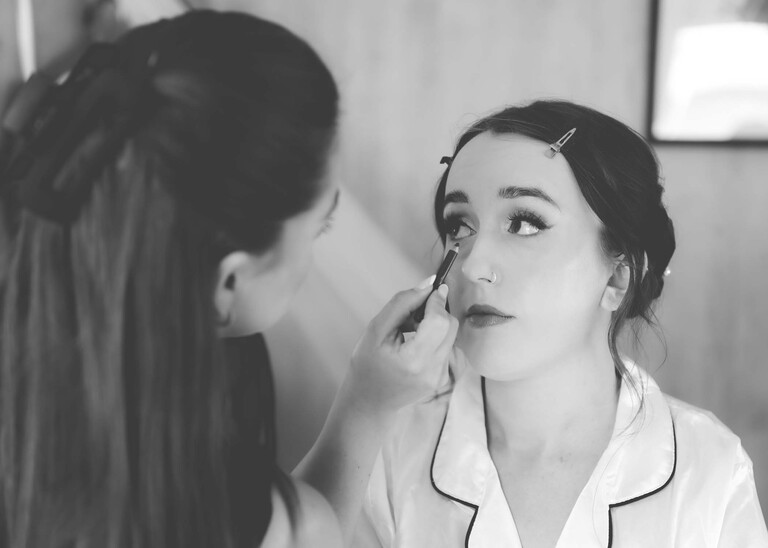 A black and white photo of a make up artist doing a brides eye make up on a wedding day at Applewood Hall in Norfolk captured by suffolk and norfolk wedding photographer Hayley Denston Photography