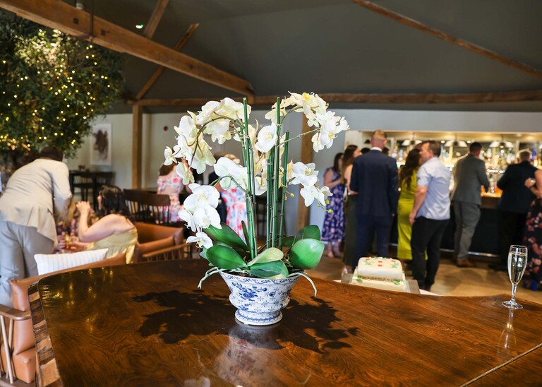 An orchid plant and an indoor wedding reception on a wedding day at Easton Grange captured by Suffolk Wedding Photographer Hayley Denston Photography