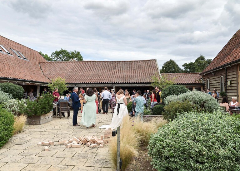 Outdoor guests mingling outside a barn on a wedding day at Easton Grange captured by Suffolk Wedding Photographer Hayley Denston Photography