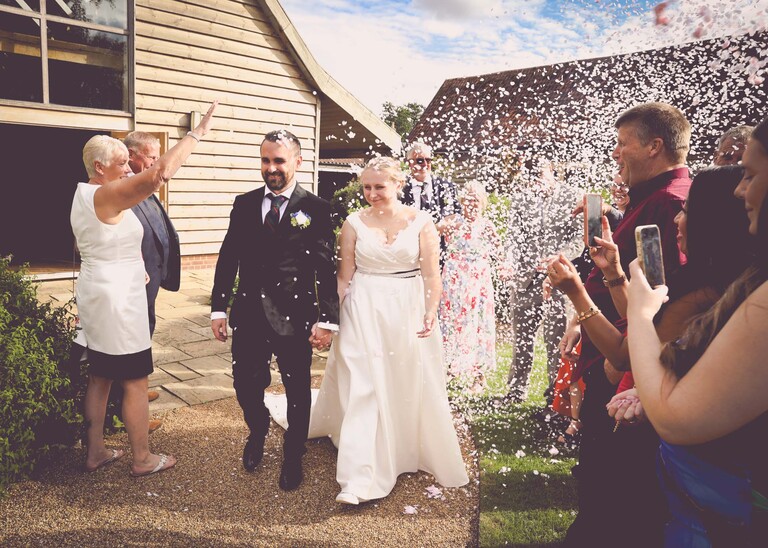 A bride and groom walking through a confetti aisle on a wedding day at Easton Grange captured by Suffolk Wedding Photographer Hayley Denston Photography