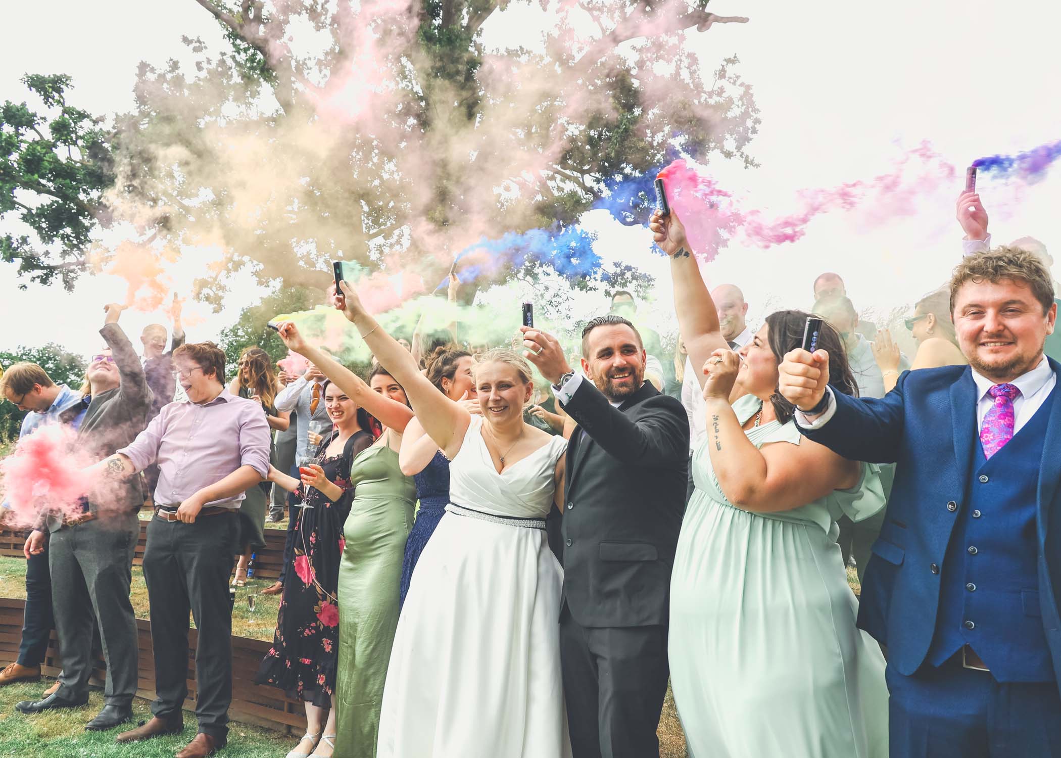 Rainbow coloured smoke bombs being fired by guests and the couple on a wedding day at Easton Grange captured by Suffolk Wedding Photographer Hayley Denston Photography