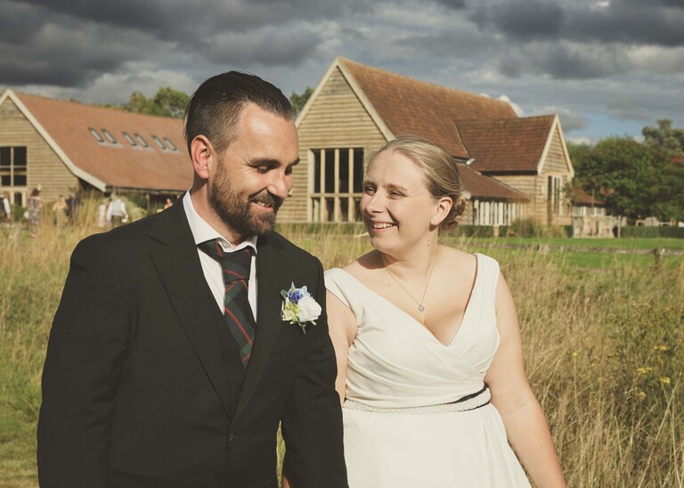 A bride and groom walking and laughing together with their wedding venue behind them on a wedding day at Easton Grange captured by Suffolk Wedding Photographer Hayley Denston Photography 