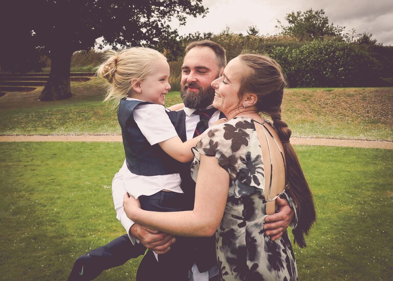 A couple and their son cuddling and all looking at each other on a wedding day at Easton Grange captured by Suffolk Wedding Photographer Hayley Denston Photography 