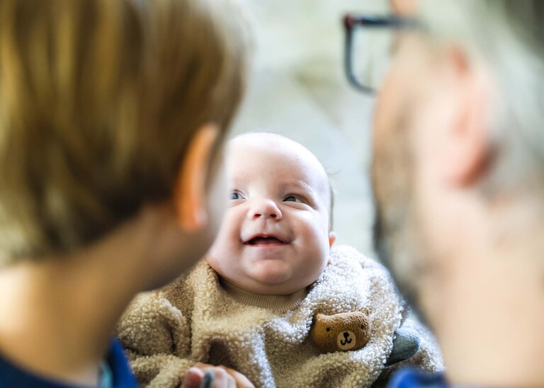 Looking over the shoulder of a young boy and his dad with a baby looking up at them smiling at their faces captured by Suffolk Portrait Photographer Hayley Denston Photography