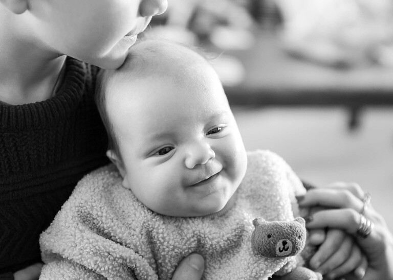 A black and white photo of a baby being cuddled by his brother  captured by Suffolk Portrait Photographer Hayley Denston Photography